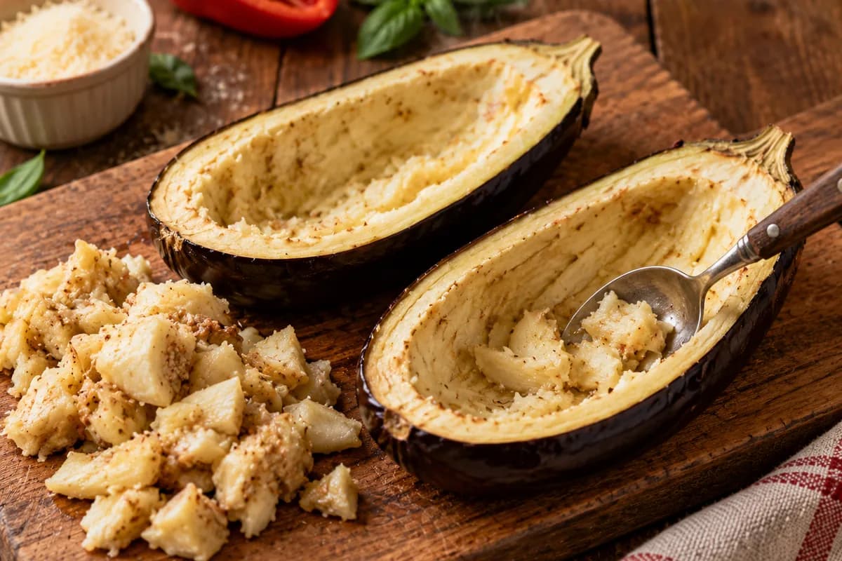 Hollowed eggplant halves with the reserved flesh on a wooden board