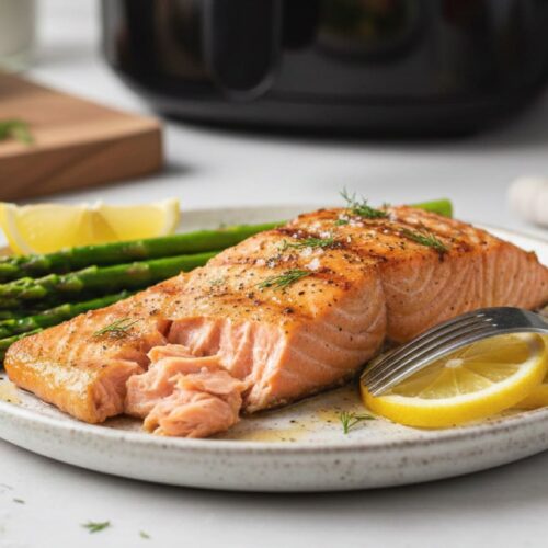 Filete de salmón en air fryer cocinado al punto con espárragos y rodajas de limón.